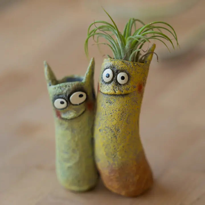 Two ceramic planters shaped like cats with googly eyes on a wooden surface.