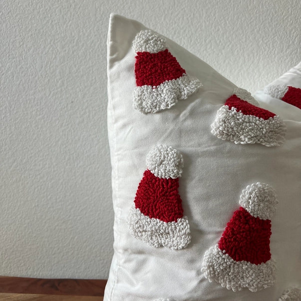 Decorative pillow with red and white textured shapes resembling Santa hats on a plain background.
