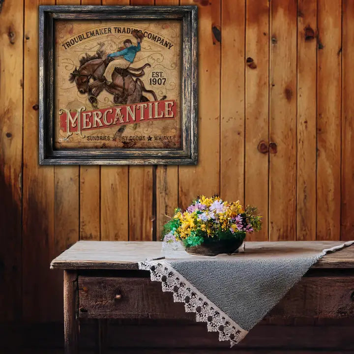 Vintage-style sign on a wooden wall above a rustic table with a floral arrangement.