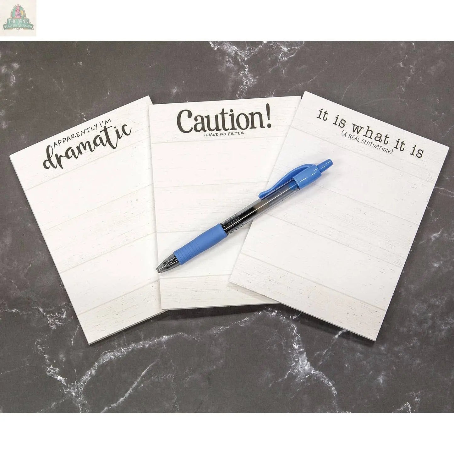 The "Apparently I'm Dramatic" notepad, featuring a humorous header, is arranged alongside two other snarky notepads on a black marble surface, with a blue pen placed on the center magnetic notepad.