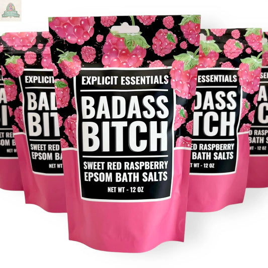 A 12oz stand-up pouch of Explicit Essentials' Bad Ass Bitch Bath Salts, featuring a black and pink raspberry-themed design, shown with similar products—a bold self-care gift.