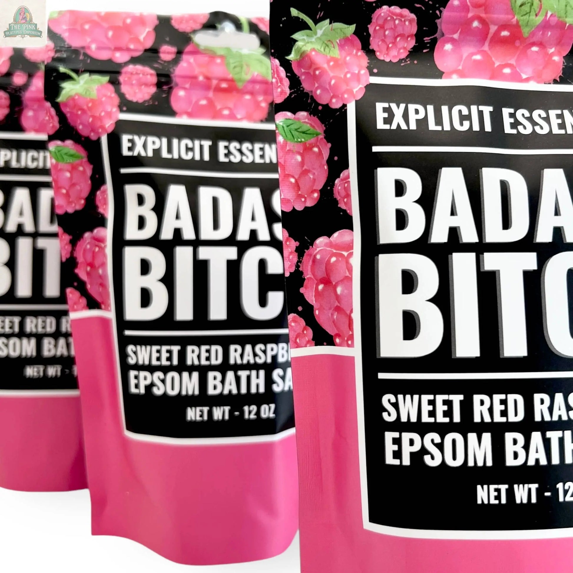 Three pink and black 12oz Bad Ass Bitch Bath Salts bags by Explicit Essentials, featuring raspberry designs—an ideal bold self-care gift.