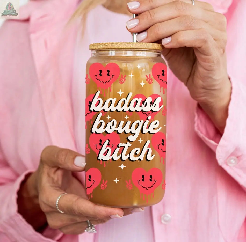 Wearing a light pink shirt, someone holds the Badass Bougie 20oz glass cup with bamboo lid and straw. Decorated with pink hearts and bold "Badass Bougie Bitch" text, it’s a standout addition to your drinkware lineup.