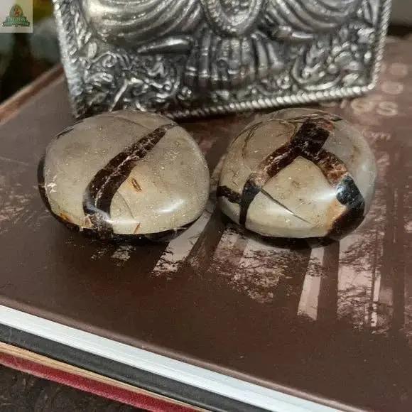 Two Beautiful Palm Dragon Stone Druzy stones from Bodhi Crystal Magic, each 2 inches wide with brown and beige patterns, rest on a closed book with a decorative silver box behind them.