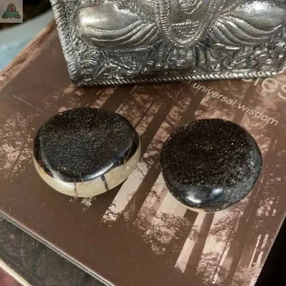 Two 2-inch round, polished Beautiful Palm Dragon Stone Druzys from Bodhi Crystal Magic rest on a book with a forest cover, near a decorative silver object with an embossed figure.