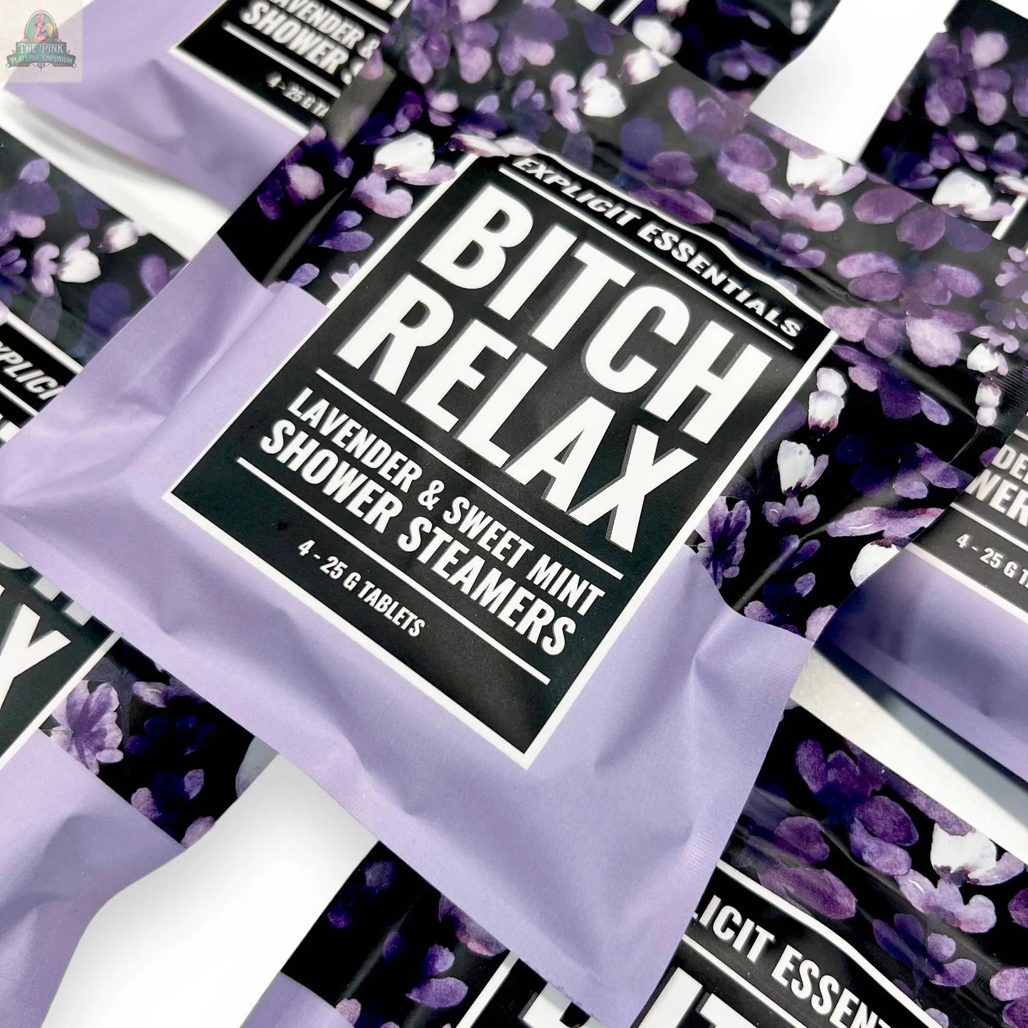 A close-up of a Bitch Relax Shower Steamers packet by Explicit Essentials, featuring lavender & sweet mint with a purple floral design; perfect for self-care. Similar relaxation shower steamers appear in the background.