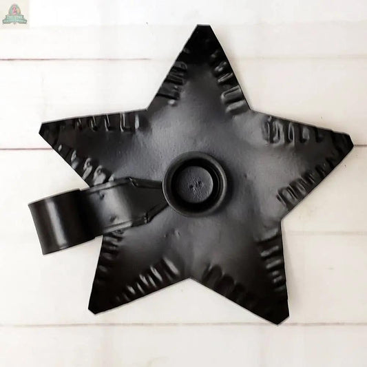 The Black Metal Star Taper Holder features a star-shaped base with a handle and is displayed on a light wooden surface.