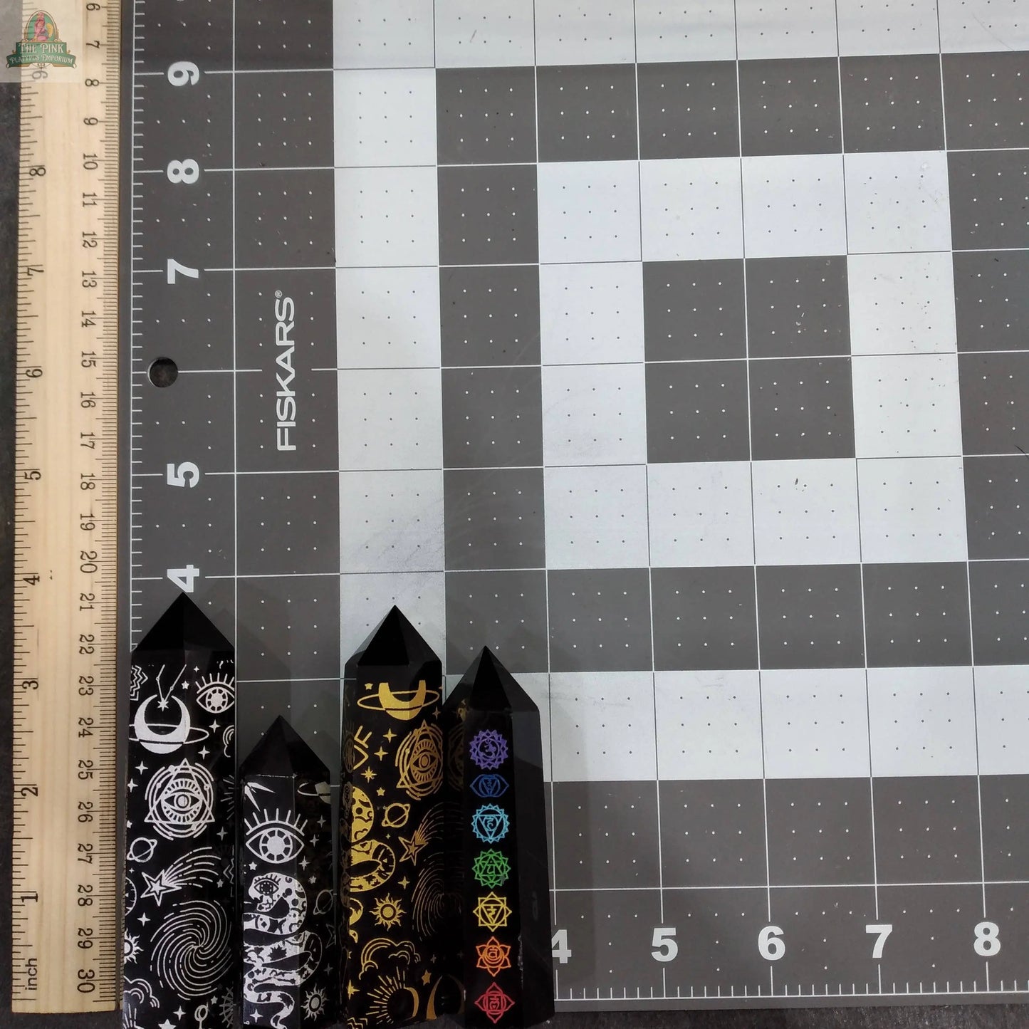 Four Keystone Crystals towers, including a Black Obsidian Chakra Obelisk from Pink Platypus Emporium, stand on a cutting mat near the 0-inch mark of a ruler. Both the mat and the ruler display inch measurements along their edges.