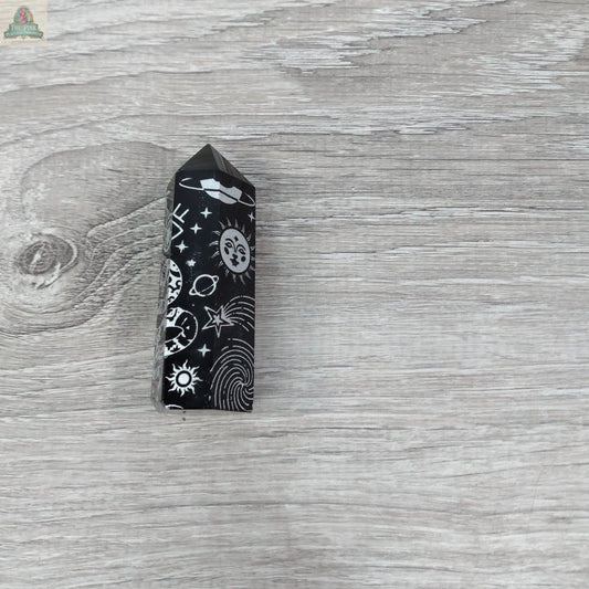 The Black Obsidian Etched Obelisk – Celestial Engraved Crystal Tower by Keystone Crystals features white sun, moon, star, and planet engravings, radiating protective energy and cosmic elegance from Pink Platypus Emporium.
