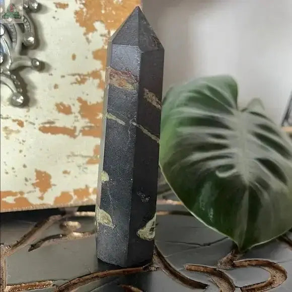 A Black and Green Hematite and Chrysoprase Obelisk Stone Decor sits elegantly on the table, making a striking crystal accent.