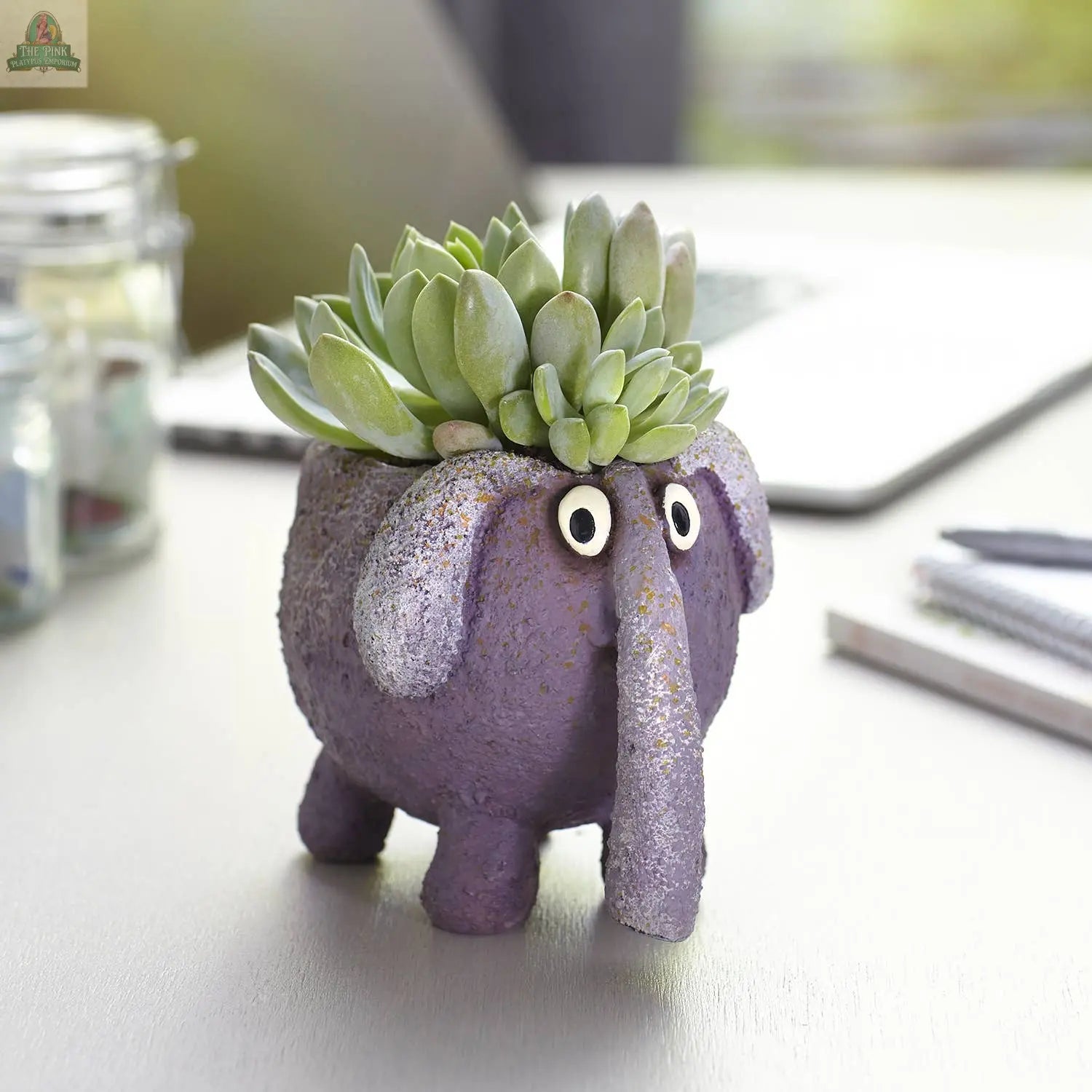 BoBo the Elephant Blobhouse Planter by Blob House Planters, a small purple pot with googly eyes and green succulents, adds whimsy to a light desk decorated with office supplies.