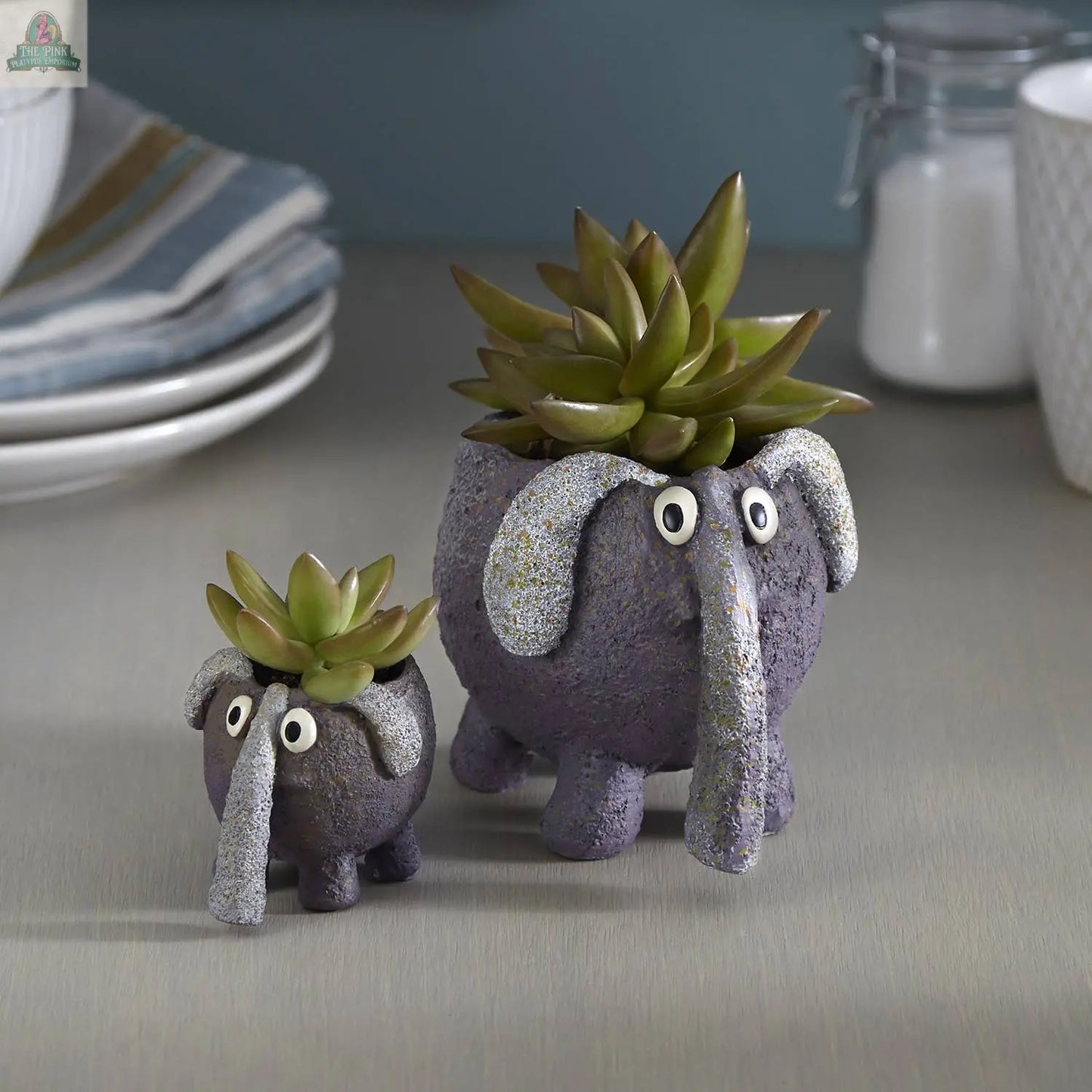 Two BoBo the Elephant Blobhouse Planters by Blob House Planters, crafted with textured material, hold succulents. The larger planter has glittery silver tusks and trunk; both feature googly eyes and sit on a light gray surface.