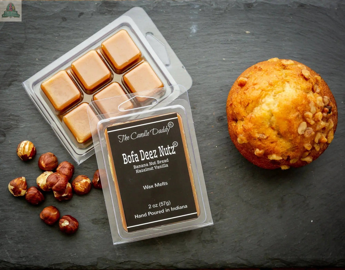 A pack of Bofa Deez Nutz Wax Melts - Banana Nut Bread sits on a slate surface beside a muffin, hazelnuts, and an open tray revealing six caramel-colored, hand-poured scented wax melts.
