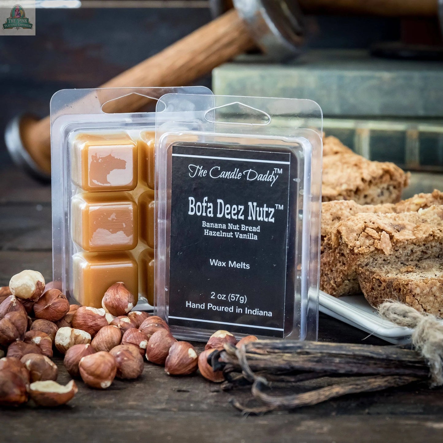 A pack of Bofa Deez Nutz Wax Melts - Banana Nut Bread sits on a rustic table with hazelnuts, banana bread, vanilla beans, and old books in the background.