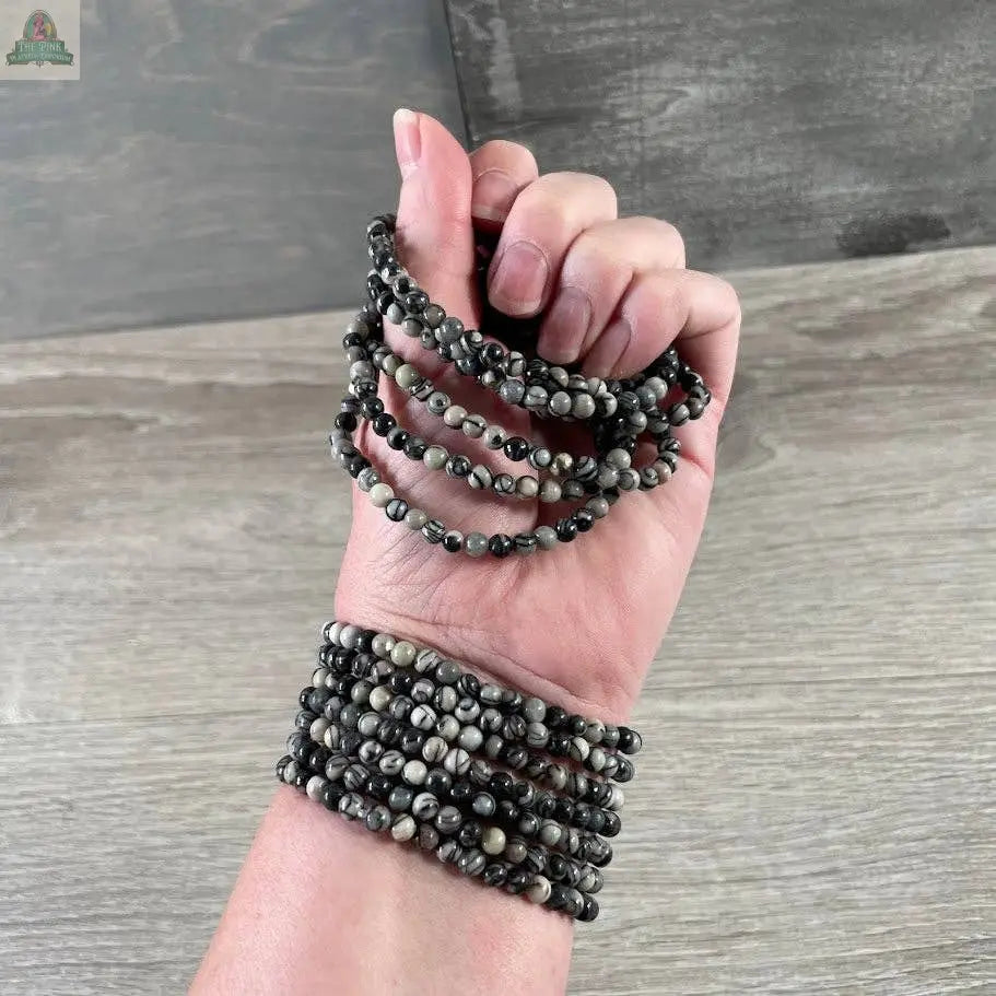 A hand wearing multiple Keystone Crystals gemstone bead bracelet 4mm—Genuine Healing Crystal Jewelry by Pink Platypus Emporium, shown against a wood background.