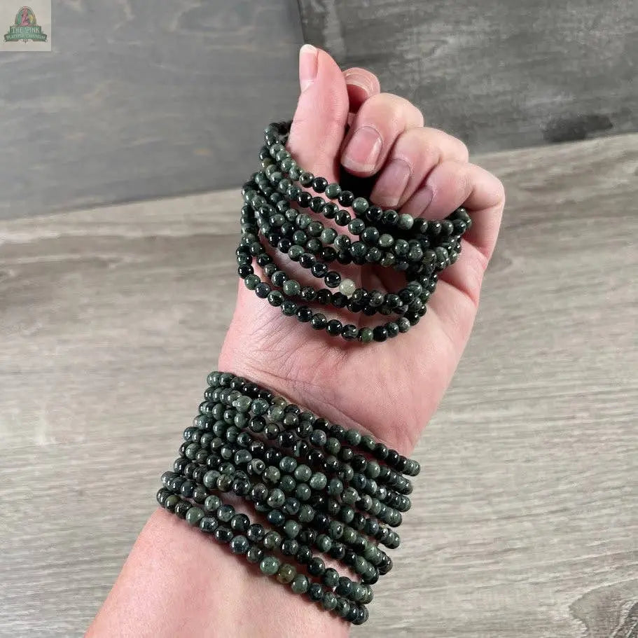 A hand wears several Keystone Crystals gemstone bead bracelets 4mm–Genuine Healing Crystal Jewelry from Pink Platypus Emporium, perfect for crystal healing enthusiasts.