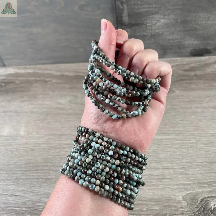 A hand and wrist adorned with a Keystone Crystals gemstone bead bracelet 4mm—genuine healing crystal jewelry from Pink Platypus Emporium—elegantly showcased on wood, ideal for lovers of natural stone accessories.