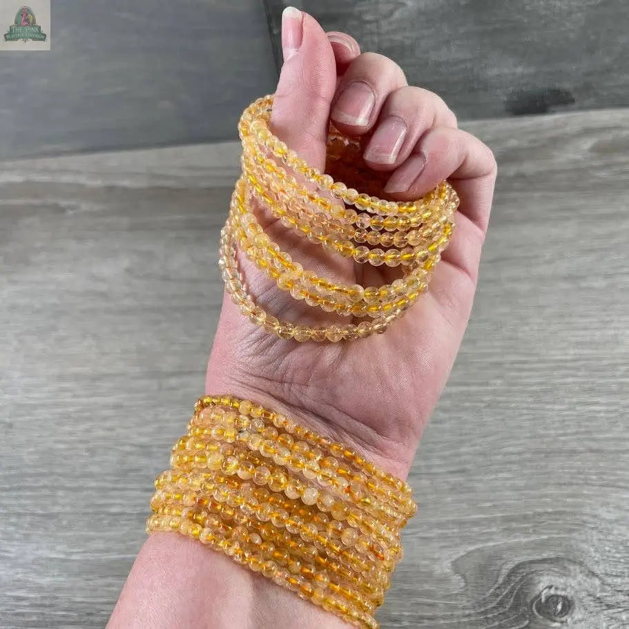 A hand and wrist showcase Keystone Crystals' 4mm gemstone bead bracelet—genuine healing crystal jewelry from Pink Platypus Emporium—featuring multiple strands of small, round beads displayed on a wooden surface.