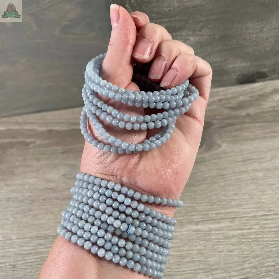 A hand adorned with several Keystone Crystals' 4mm gemstone bead bracelets from Pink Platypus Emporium, featuring genuine healing crystals, is wrapped around the wrist and fingers against a wooden backdrop.