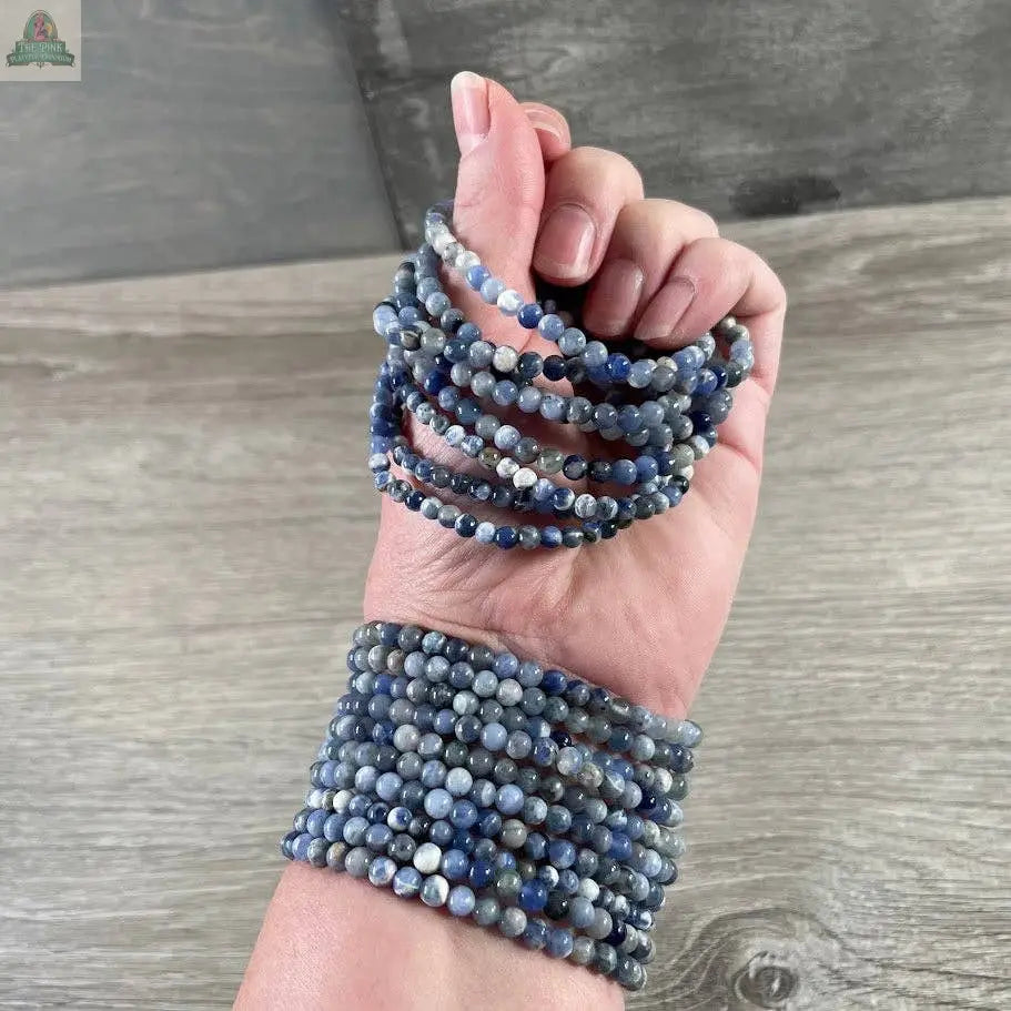 A hand and wrist adorned with the Keystone Crystals gemstone bead bracelet 4mm – Genuine Healing Crystal Jewelry from Pink Platypus Emporium, shown against a wooden background.