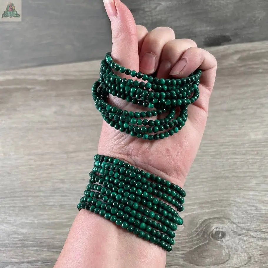 A hand wearing multiple strands of Keystone Crystals gemstone bead bracelet 4mm–Genuine Healing Crystal Jewelry from Pink Platypus Emporium, wrapped around the wrist and fingers, set against a wooden background.