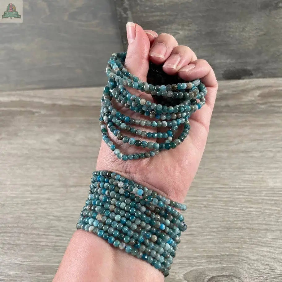A hand wearing the Keystone Crystals gemstone bead bracelet 4mm from Pink Platypus Emporium, featuring genuine healing crystal beads, is displayed against a wooden surface background.