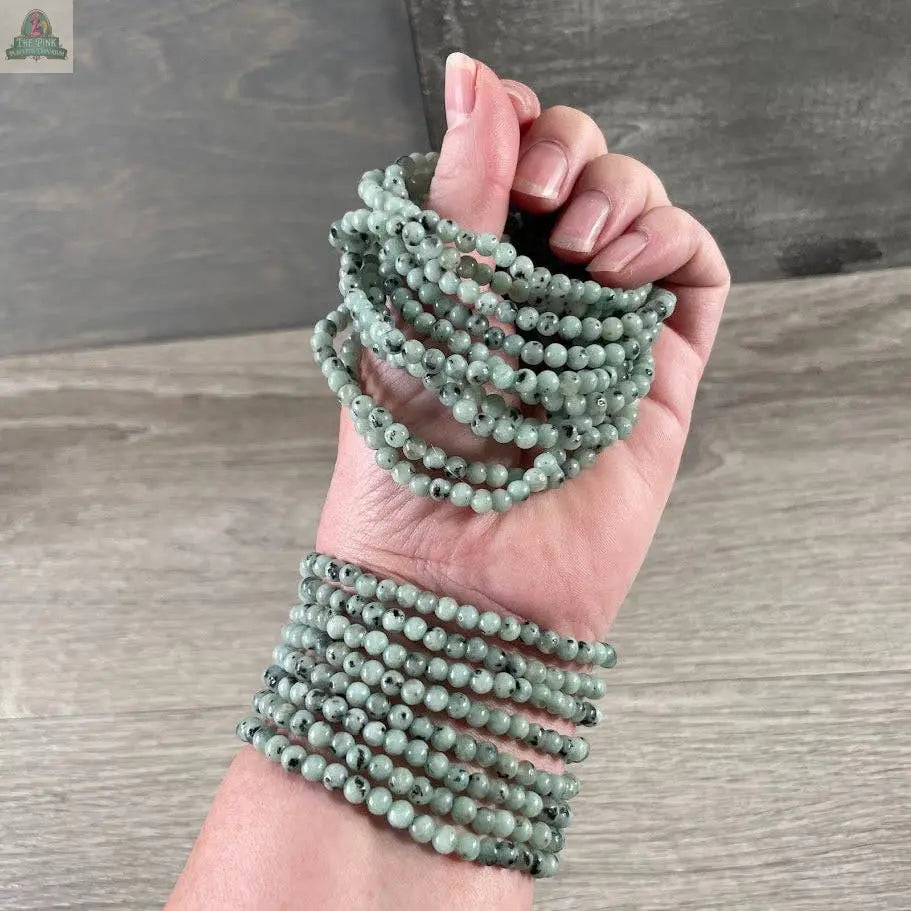 A hand and wrist display the Keystone Crystals gemstone bead bracelet 4mm—Genuine Healing Crystal Jewelry from Pink Platypus Emporium, featuring smooth, uniform round beads for a stylish crystal healing touch against a wooden background.