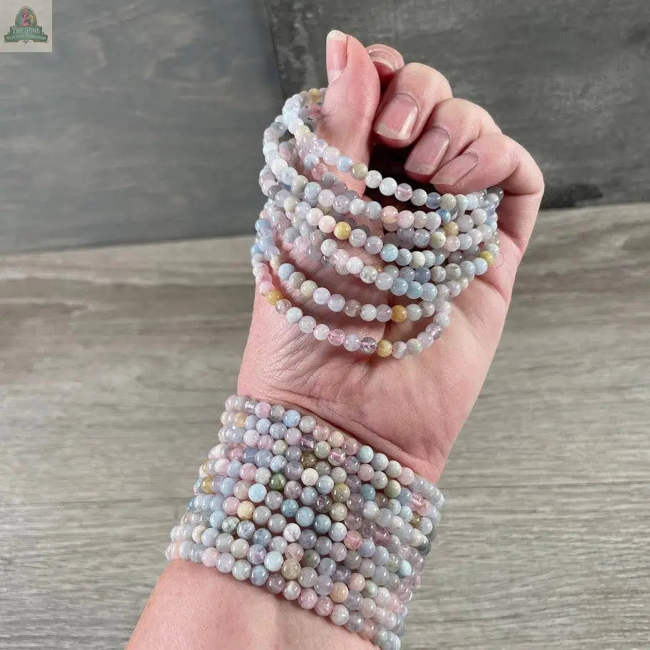 A hand displays Keystone Crystals' 4mm gemstone bead bracelet—genuine healing crystal jewelry from Pink Platypus Emporium—paired with natural stone bracelets, set against a neutral wooden background to highlight their beauty.
