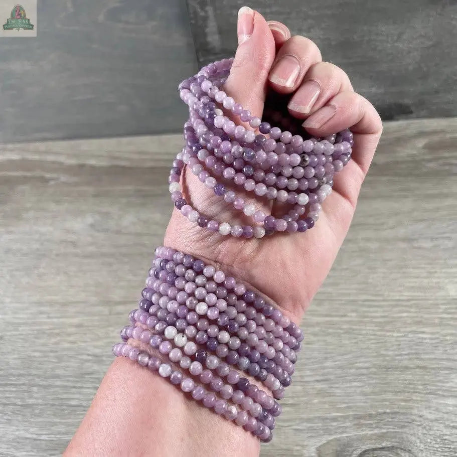 A hand with light pink nail polish displays several Keystone Crystals gemstone bead bracelet 4mm–Genuine Healing Crystal Jewelry from Pink Platypus Emporium, wrapped around the wrist and fingers against a neutral wooden background.