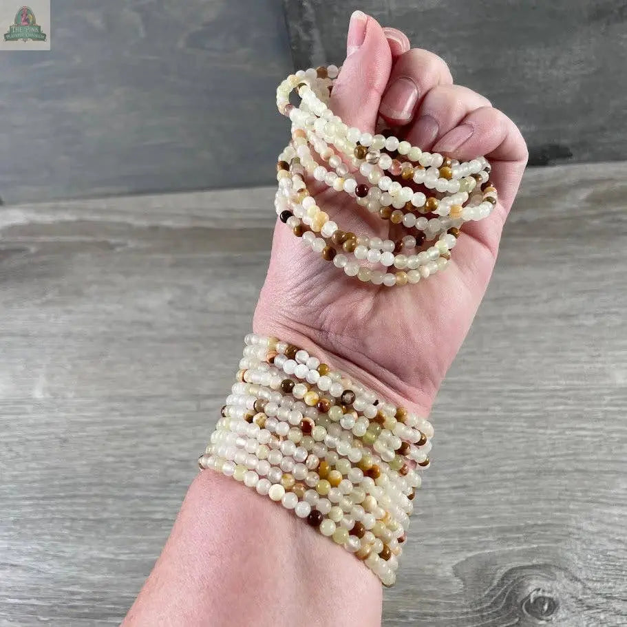 A hand displays several Keystone Crystals gemstone bead bracelet 4mm—Genuine Healing Crystal Jewelry from Pink Platypus Emporium, their multicolored beads wrapped stylishly around the wrist against a wooden background.
