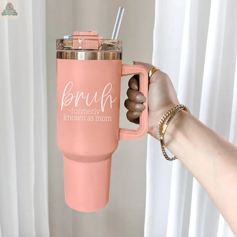 A manicured hand with gold bracelets holds the Bruh Pink 40oz tumbler with handle, featuring "bruh - formerly known as mom" in white text. White curtains are in the background—perfect for a fun mom gift.
