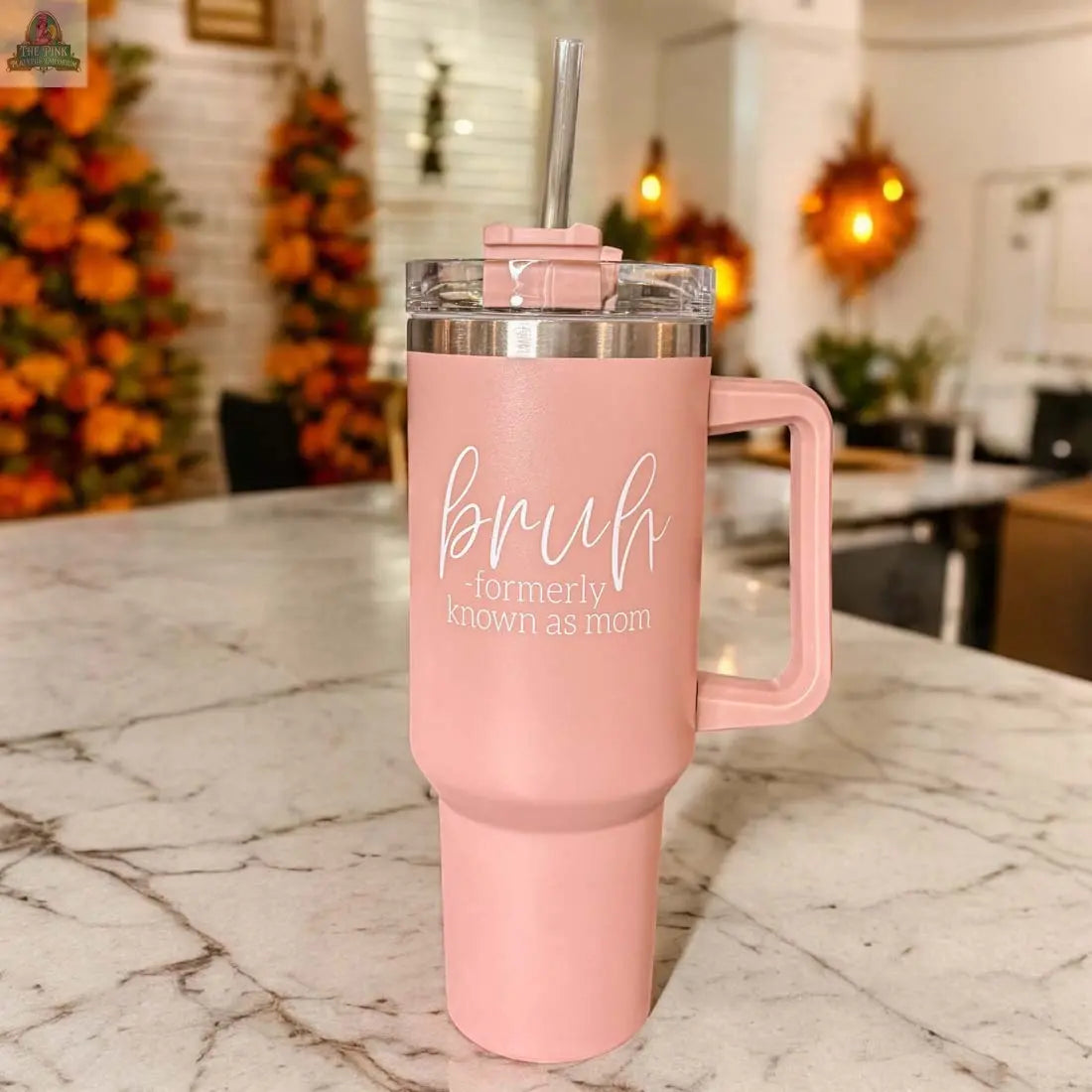 A Bruh Pink 40oz tumbler with handle and straw sits on a marble counter. “bruh - formerly known as mom” is printed in white, making it a perfect mom gift. Autumn decor appears blurred in the background.