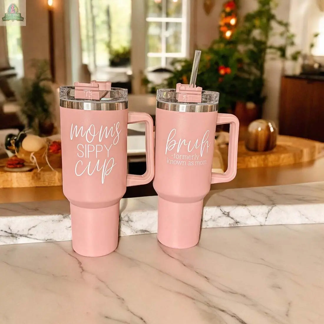 Two Bruh Pink 40oz tumblers with handles rest on a marble counter; one says "mom's sippy cup," the other "Bruh Formerly Known as Mom." Ideal gift for moms, these tumblers add style and fun to any kitchen.
