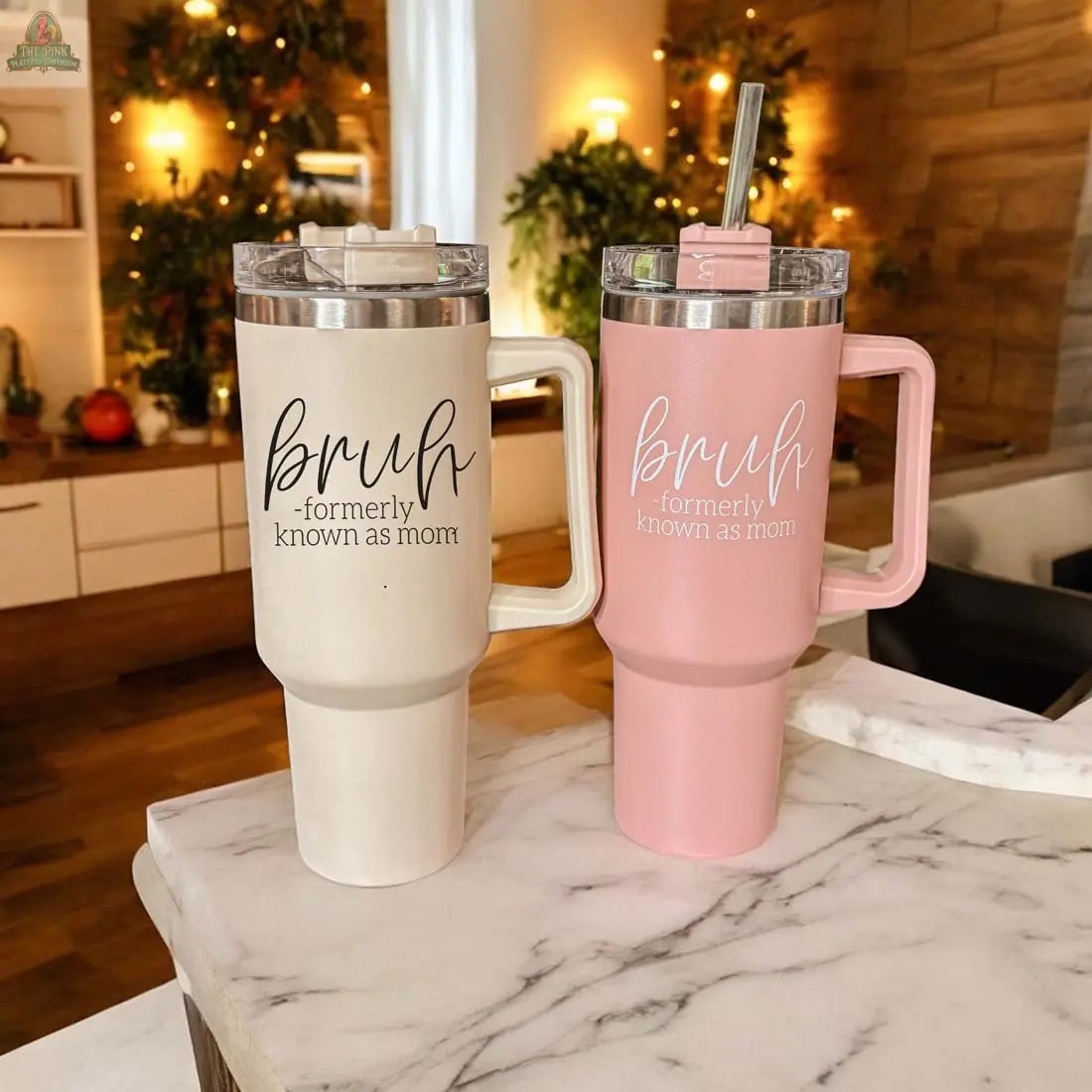 The Bruh Pink 40oz mug sits on a marble counter, featuring the phrase "bruh - formerly known as mom." This unique mom gift adds a charming touch to any warmly lit, festive kitchen.