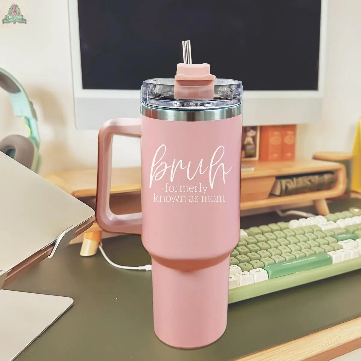 The Bruh Pink 40oz tumbler with handle and straw sits on a desk in front of a computer, shown alongside a keyboard and headphones. This funny mom gift is perfect for any workspace.