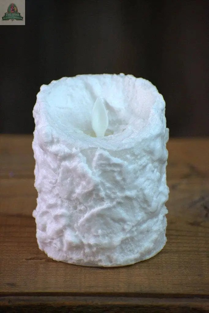 The Bumpy White Moving Flame LED Candle (3in x 4in) features a textured, uneven surface, offering an elegant flameless decor piece that sits beautifully on any wooden surface against a dark, blurred backdrop.