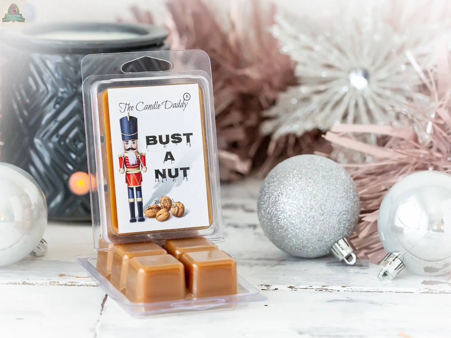 A package of Bust A Nut - Funny Christmas Banana Nut Bread Scented Wax Melts features a nutcracker, walnuts, and silver ornaments on a festive white wooden surface—ideal for banana nut bread scent lovers.