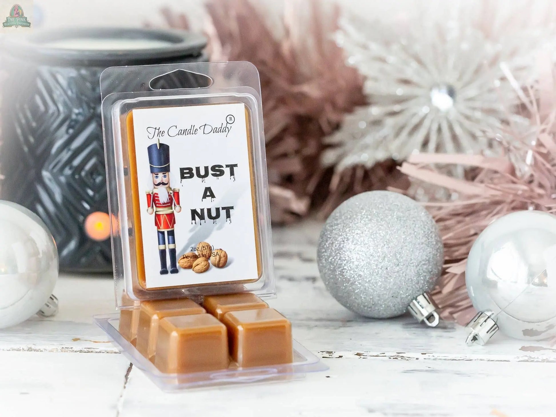 A package of Bust A Nut - Funny Christmas Banana Nut Bread Scented Wax Melts features a nutcracker, walnuts, and silver ornaments on a festive white wooden surface—ideal for banana nut bread scent lovers.