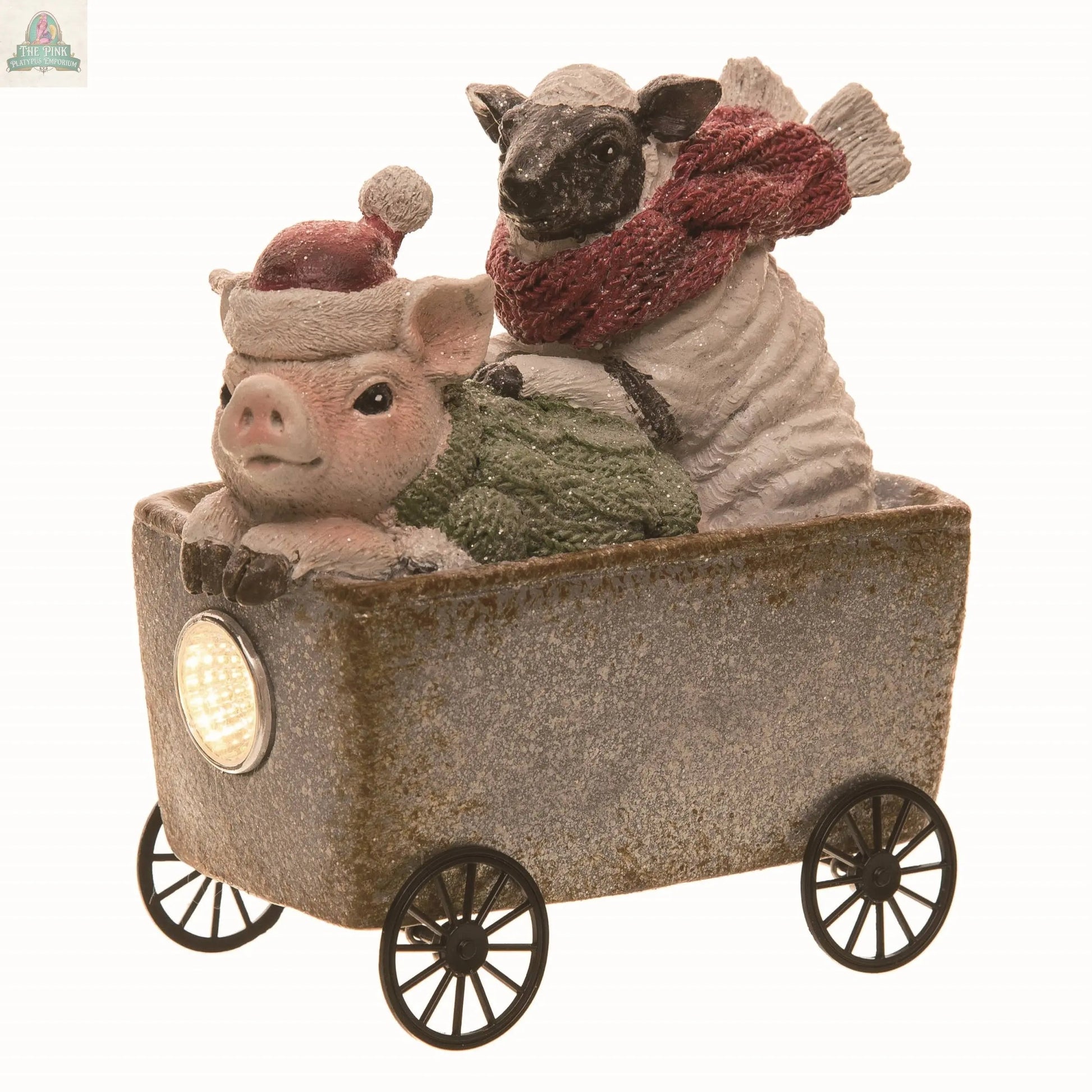 The Resin 5.51 in. Christmas Farm Figurine showcases a pig in a Santa hat and a sheep in a red scarf riding a wheeled cart with a lit headlamp, crafted in multicolor polyresin with charming rustic and handcraft details.