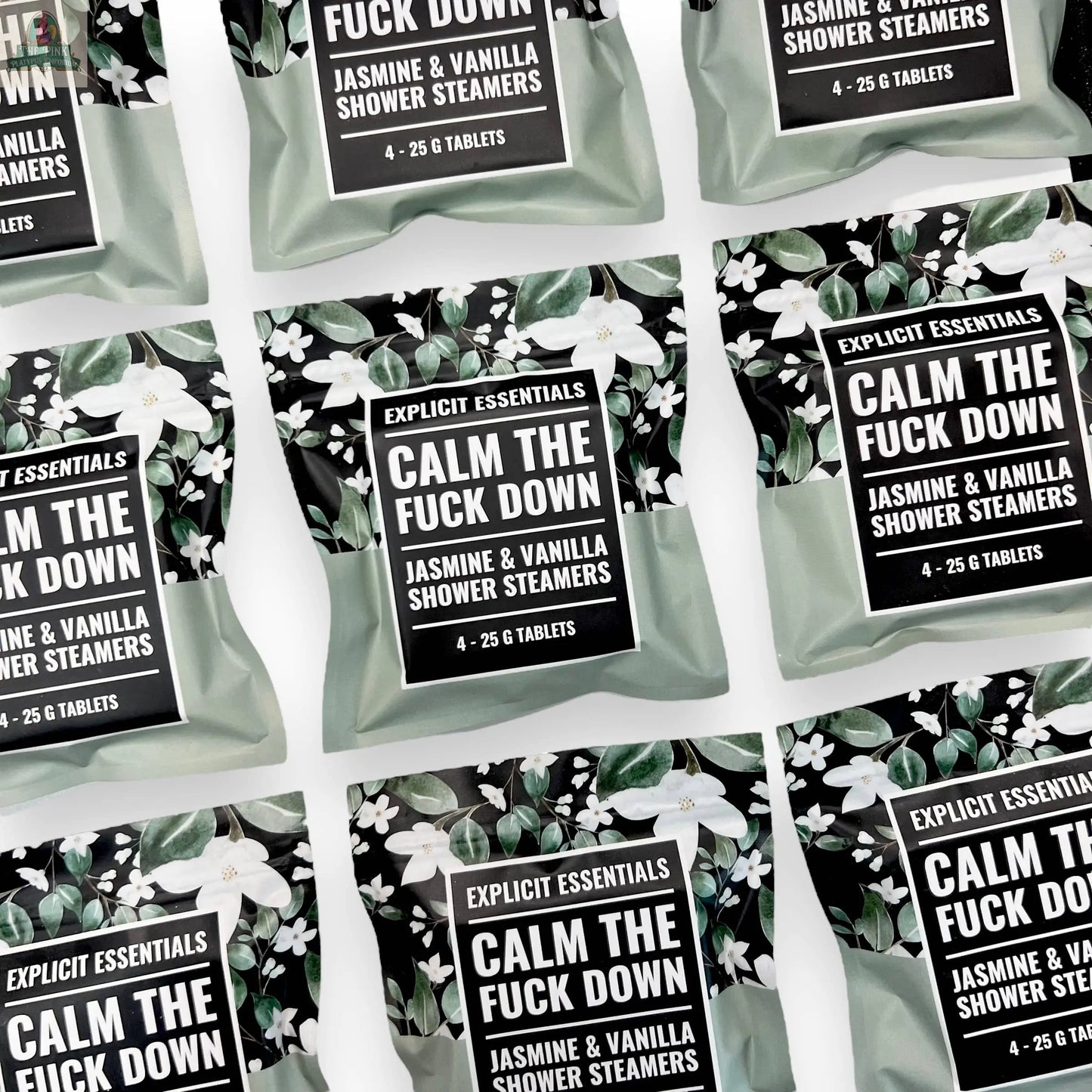 Multiple packets of Explicit Essentials Calm TF Down Shower Steamers are arranged in a flat lay on a white background. The green packaging with floral accents highlights their soothing jasmine and vanilla aromatherapy scent.