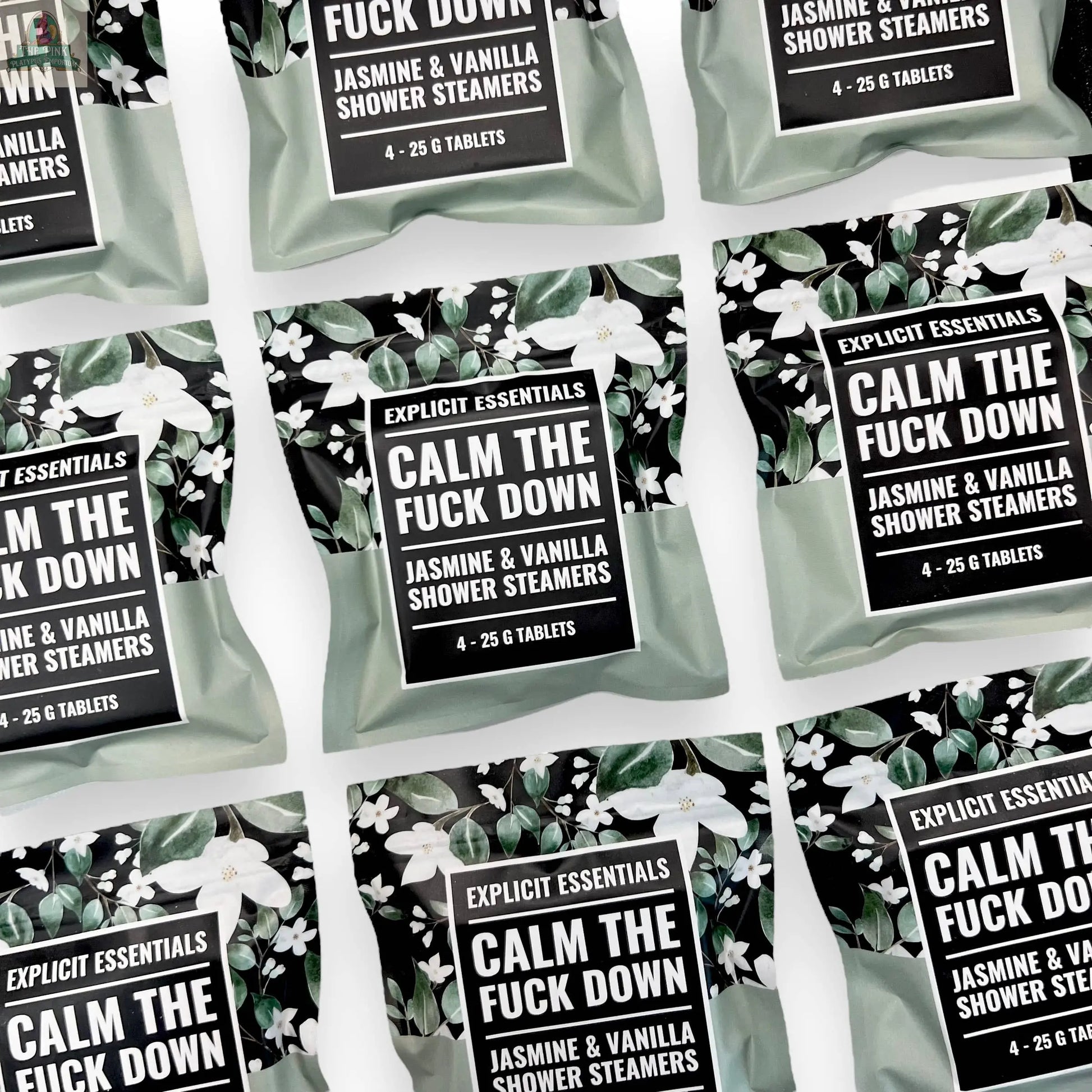 Multiple packets of Explicit Essentials Calm TF Down Shower Steamers are arranged in a flat lay on a white background. The green packaging with floral accents highlights their soothing jasmine and vanilla aromatherapy scent.
