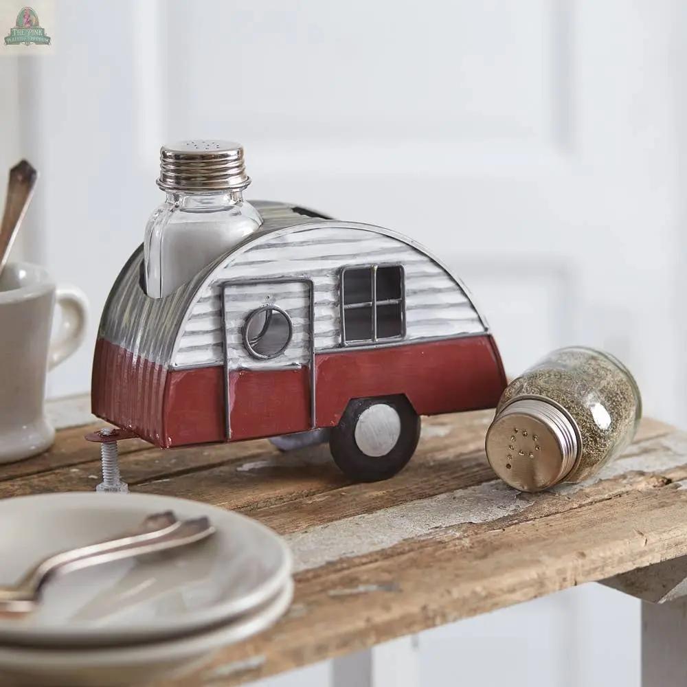 The Camper Salt and Pepper Caddy, with glass shakers shaped like a red and silver vintage camper trailer, sits on a rustic wooden table—one shaker upright on the camper, the other playfully on its side, ready for picnic grilling.