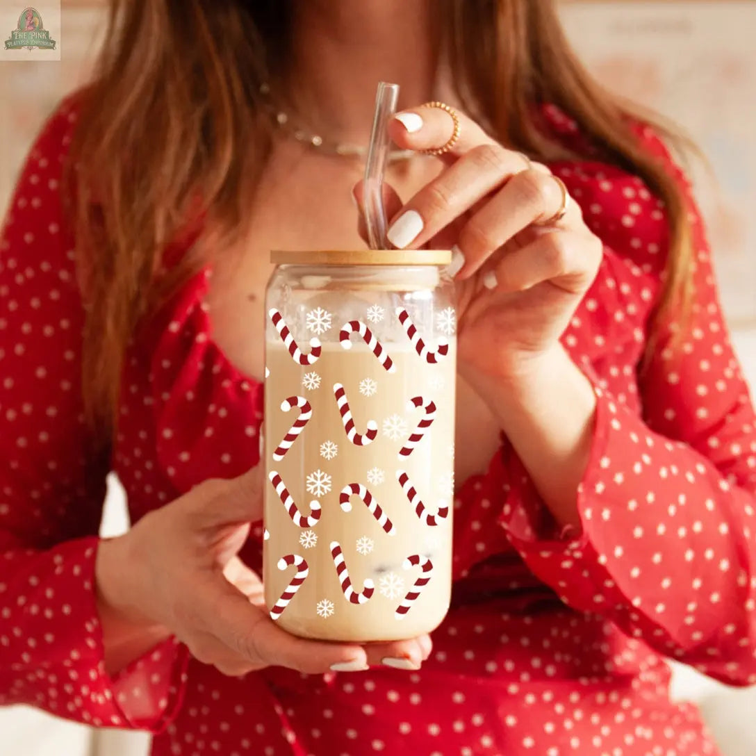 A woman in a red polka-dot dress holds the Candy Cane holiday glass cup, featuring festive candy cane and snowflake designs, with a bamboo lid and clear straw—perfect for Christmas sipping.