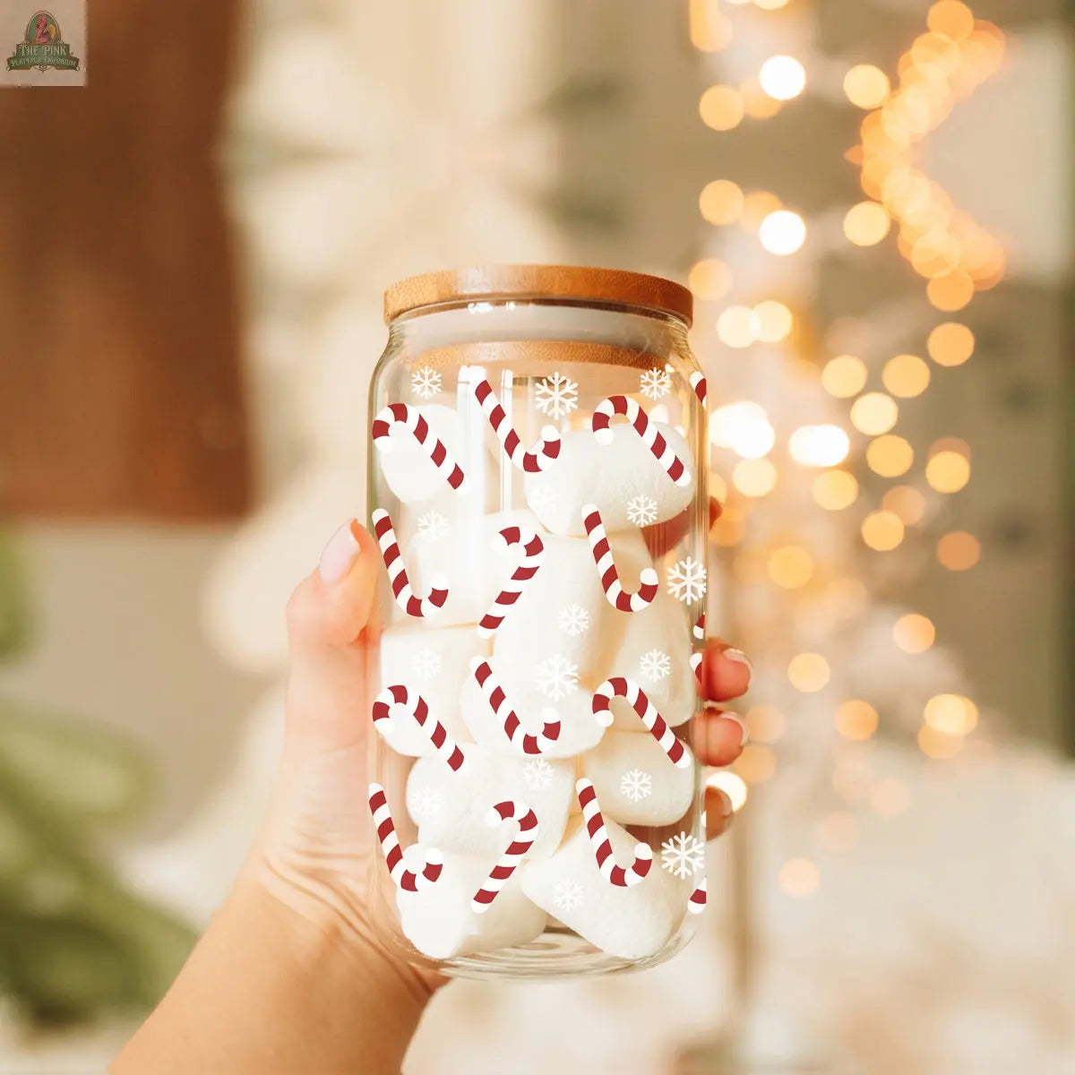 A hand holds the Candy Cane cup with a wooden lid, filled with white treats. Featuring red-and-white candy cane and snowflake designs, the mug glows amid warm, blurred holiday lights.
