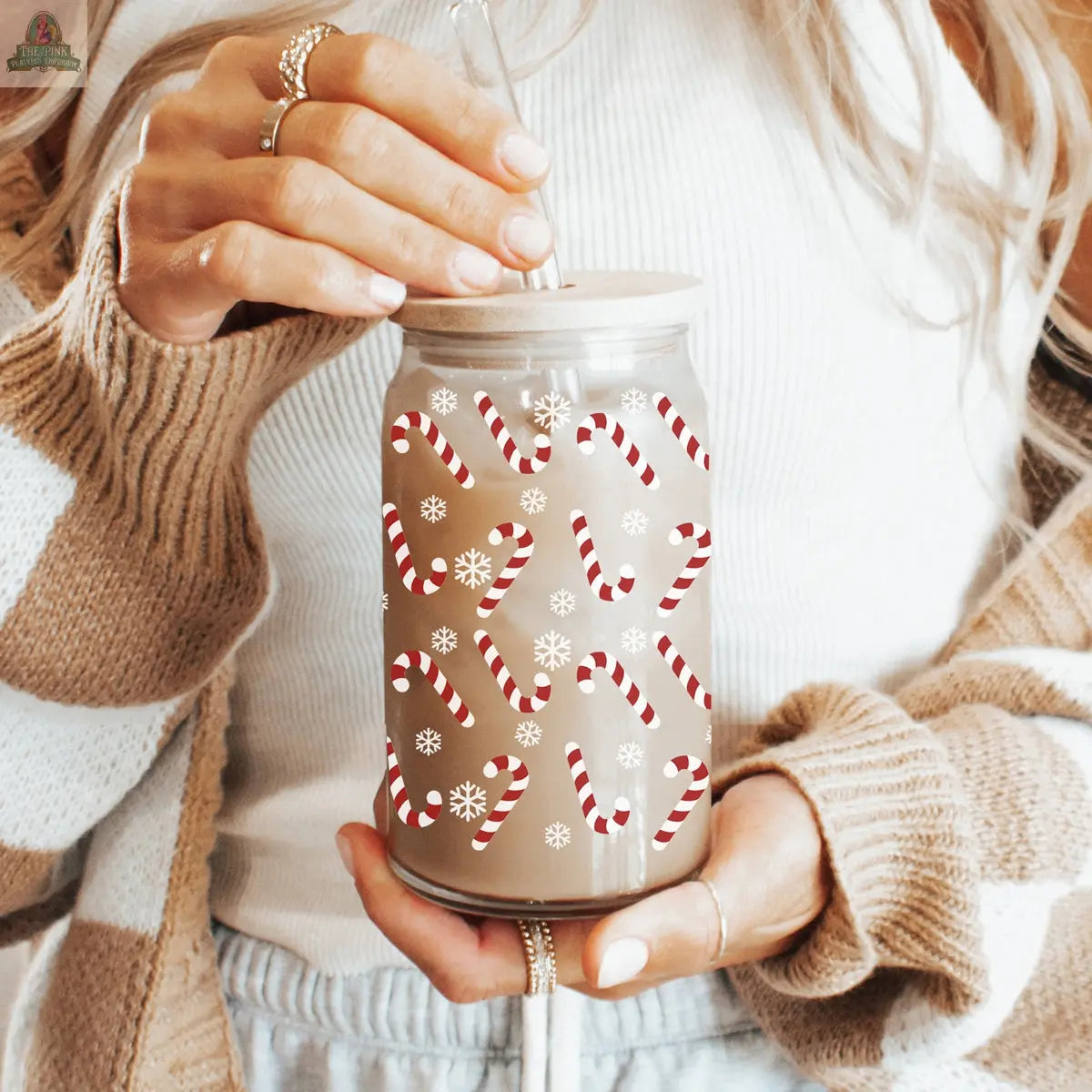 A woman in a white top and striped cardigan drinks from a straw, using the Candy Cane festive holiday glass cup decorated with red candy canes and white snowflakes.