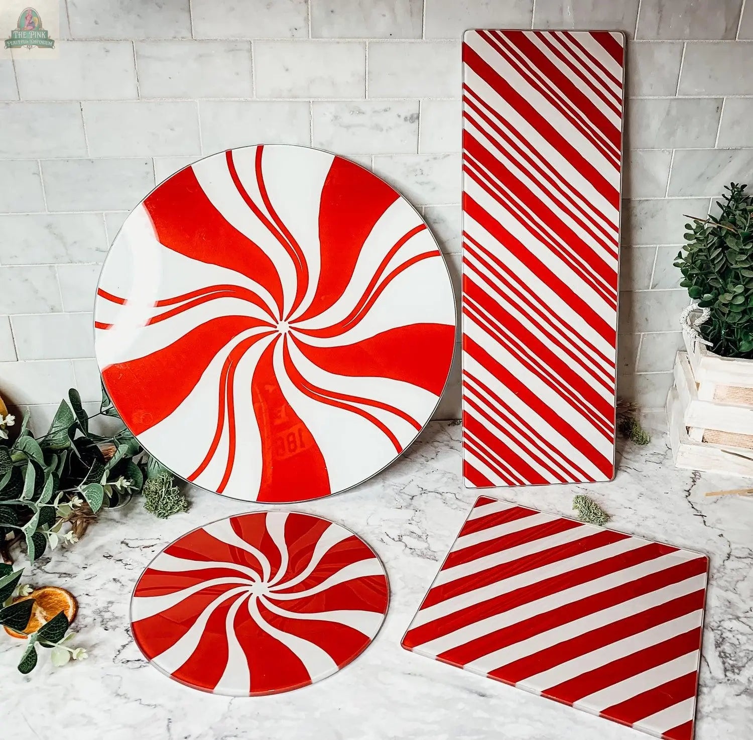 The Candy Cane Serving collection features four glass serving platters with hand-painted red and white peppermint swirls or candy cane stripes, in round, rectangular, and square shapes—perfect for festive holiday kitchen decor.
