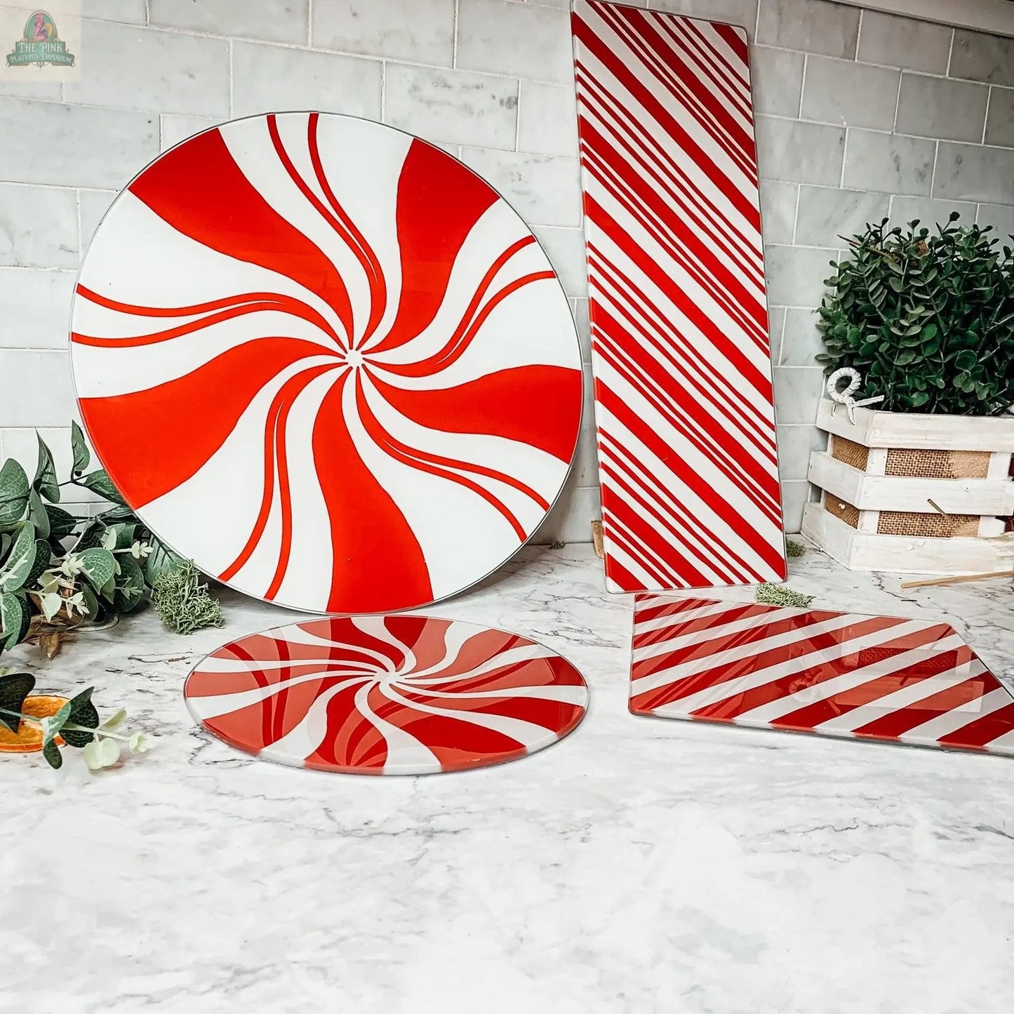 Candy Cane Serving plates and cutting boards, perfect for holiday kitchen decor, are displayed on a marble countertop with greenery and a small crate, set against a white tiled wall.