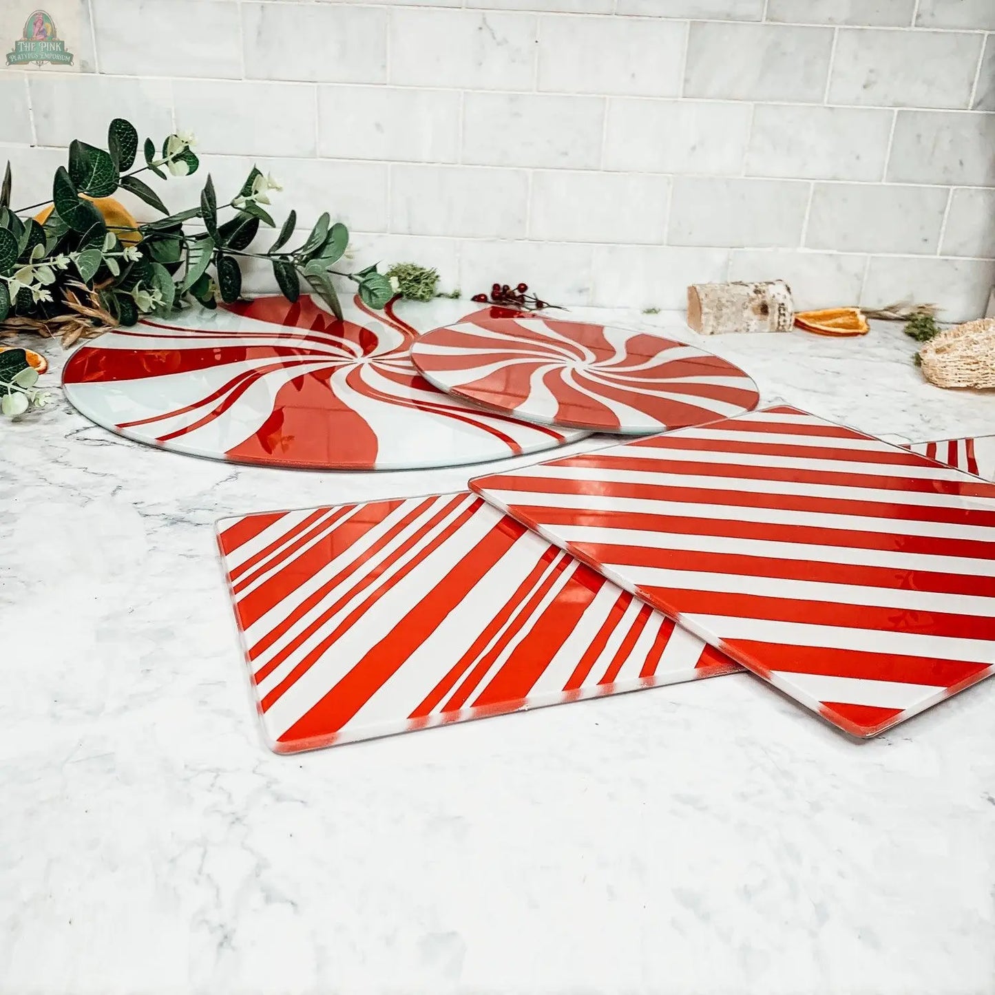 The Candy Cane Serving platter from our hand-painted glass collection brings festive flair to your holiday kitchen decor, displayed on a marble countertop with greenery and dried orange slices in the background.