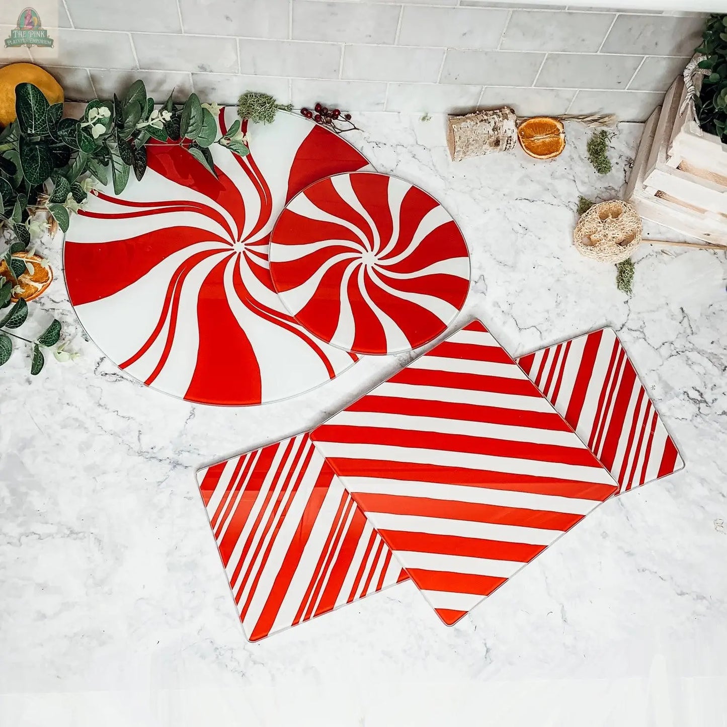 Candy Cane Serving plates, with red and white peppermint-inspired designs, arranged on a marble countertop among greenery and wooden accents—ideal for bringing festive holiday spirit to your kitchen decor.