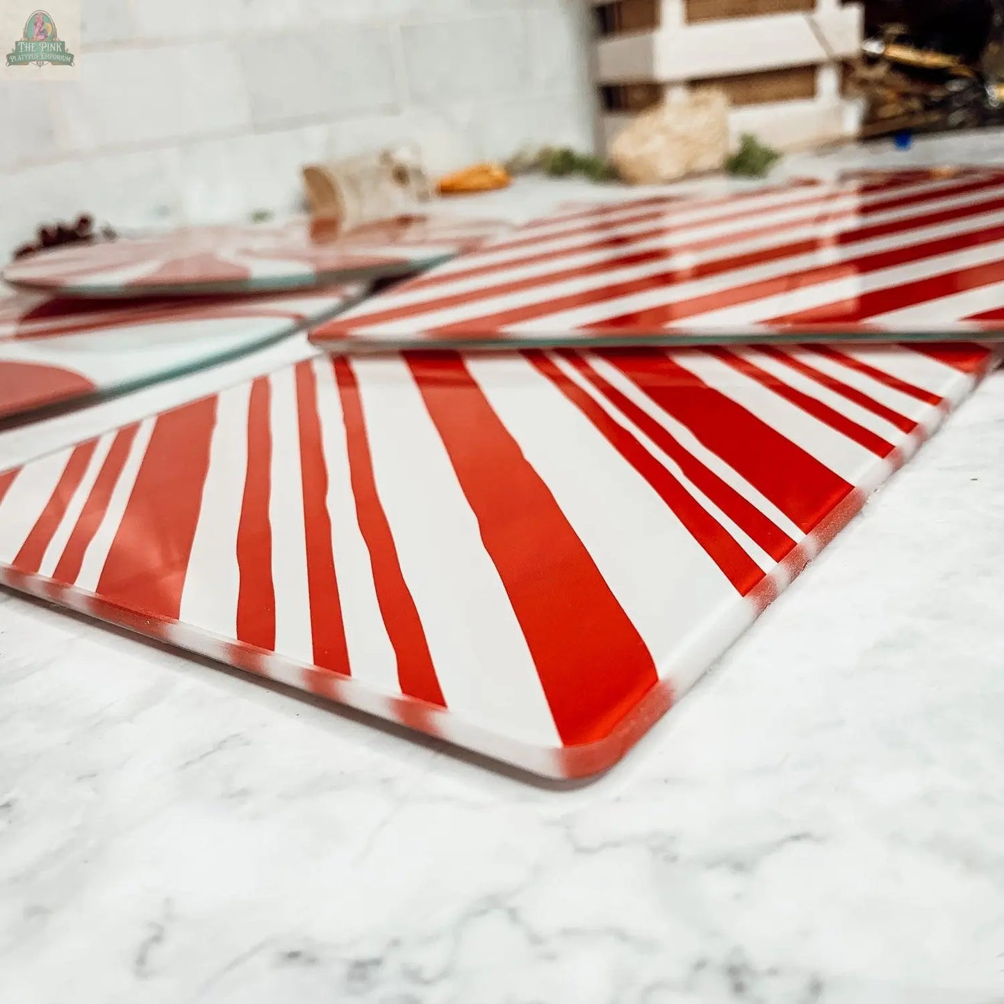 Close-up of Candy Cane Serving platters featuring red and white diagonal stripes on a marble surface. These glass platters resemble candy canes, making them perfect for festive holiday kitchen decor. Background is softly blurred.